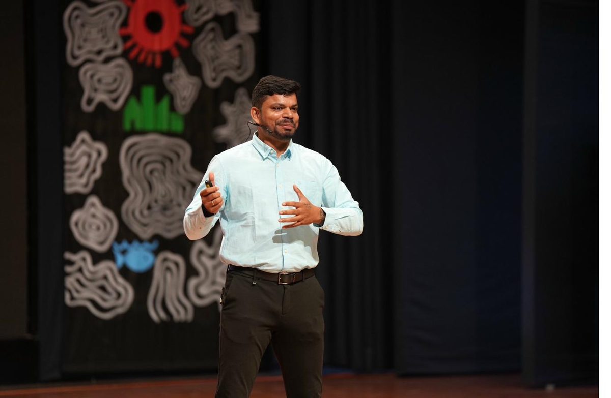 Jothi Viknesh speaking on stage with headset mic